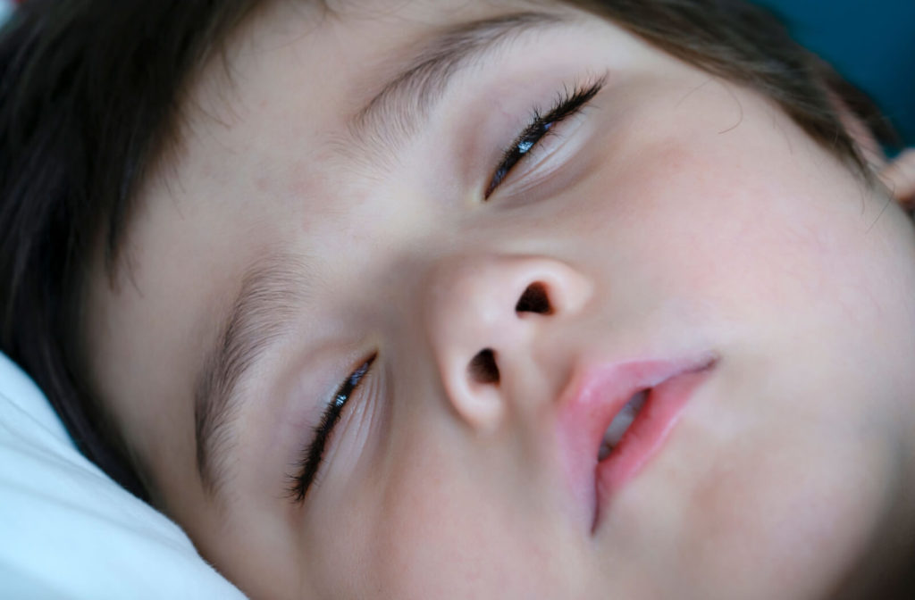 A close-up of a young boy sleeping with his eyes half open.