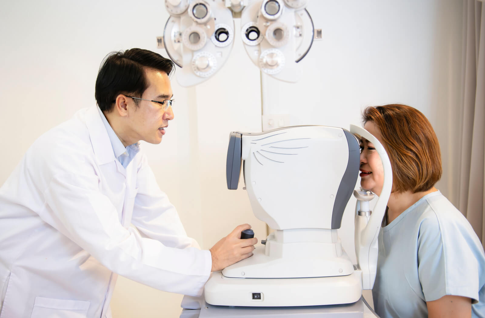 A male optometrist examines a mid-age female patient's eyesight with the use of an automated refractor machine used to determine a person's refractive error.
