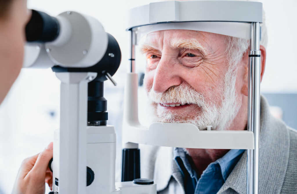 Close-up of a senior man smiling and looking into a piece of optometry equipment as his optometrist performs an eye exam