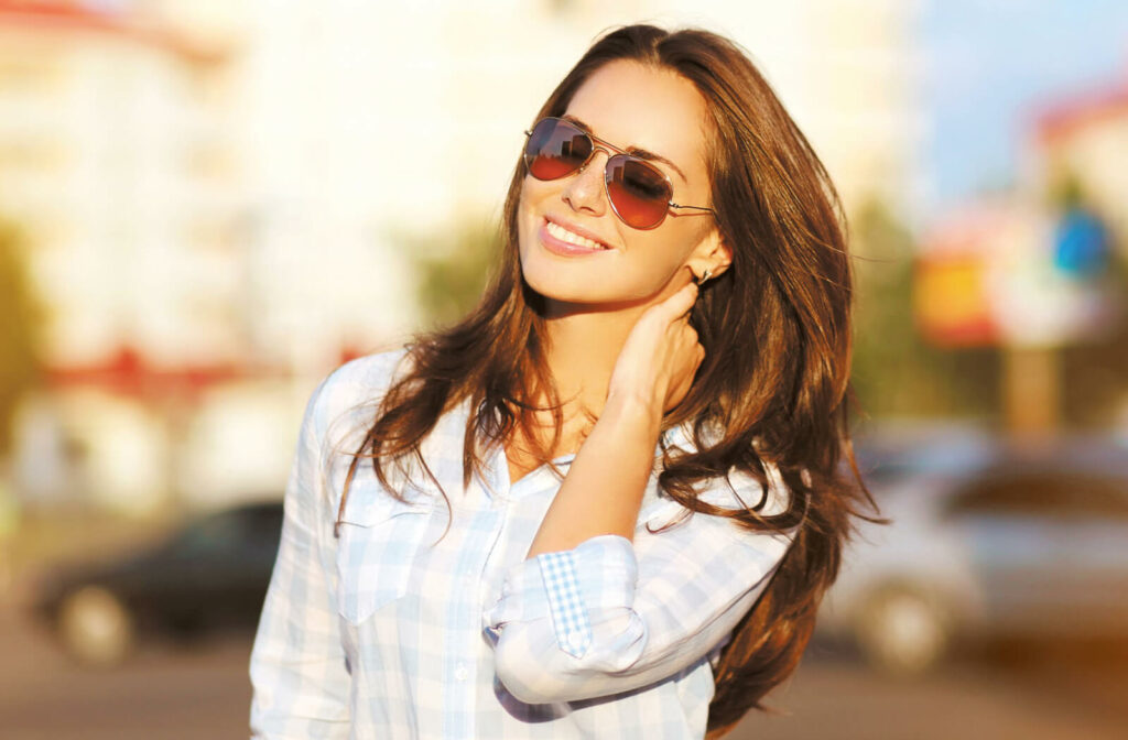 A smiling woman enjoying the sun outside while wearing sunglasses