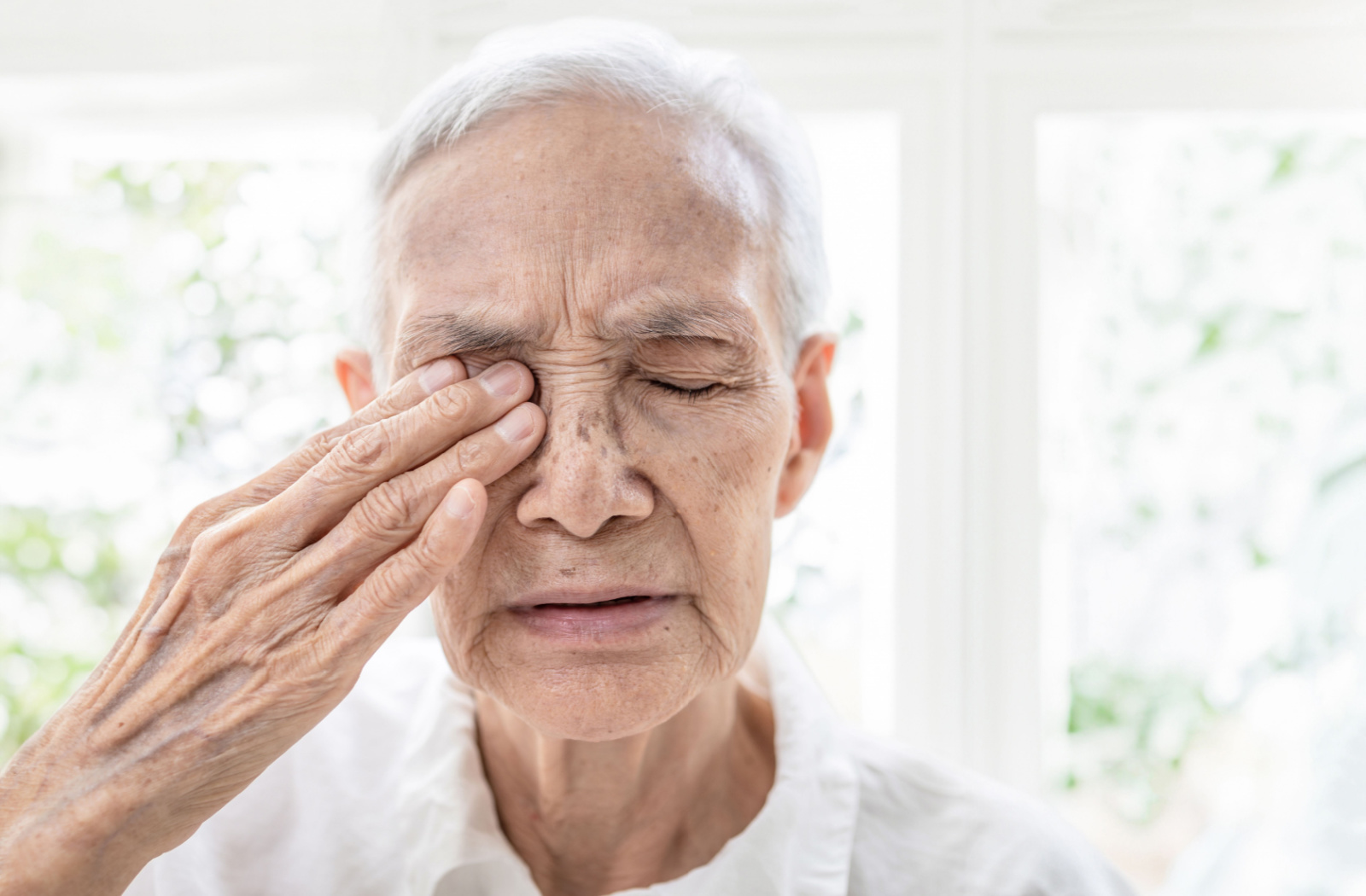 An older adult man with his eyes closed rubbing his right eye with his right hand