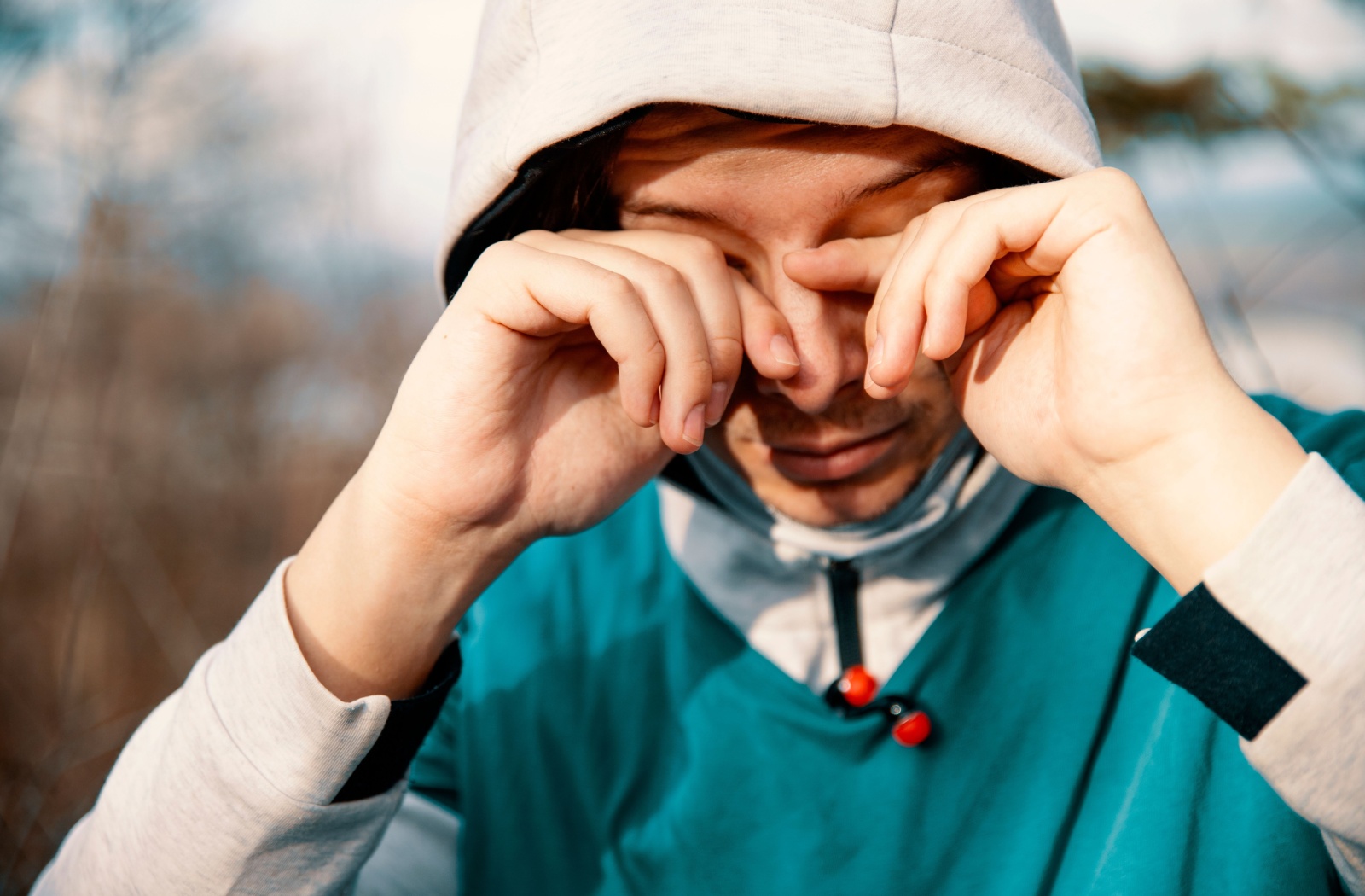 A person wearing athletic clothing outdoors rubs their eyes due to irritation and dry eye.