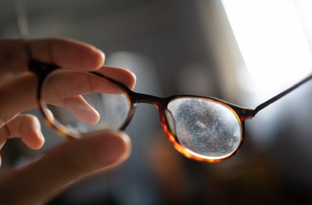 A close-up image of a pair of eyeglasses with scratched, dirty lenses over a blurry background.