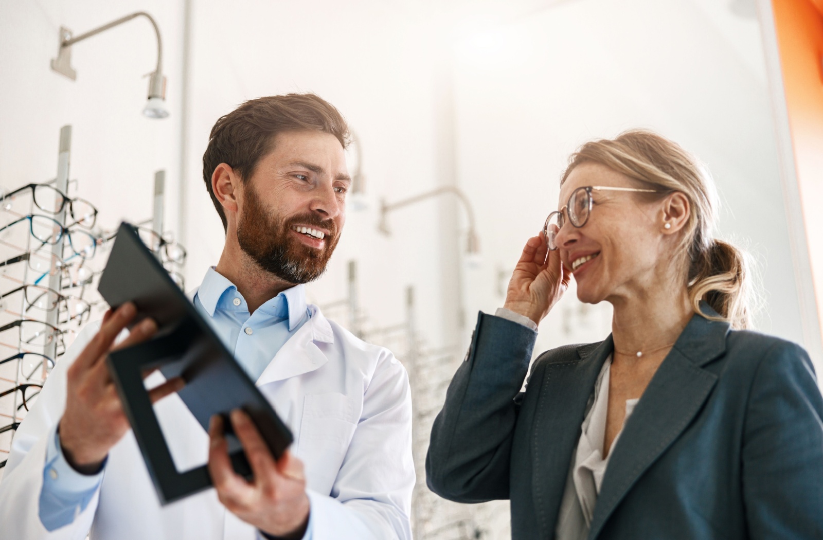 An optometrist smiling while holding up a mirror so a patient can admire her new pair of eyeglasses.