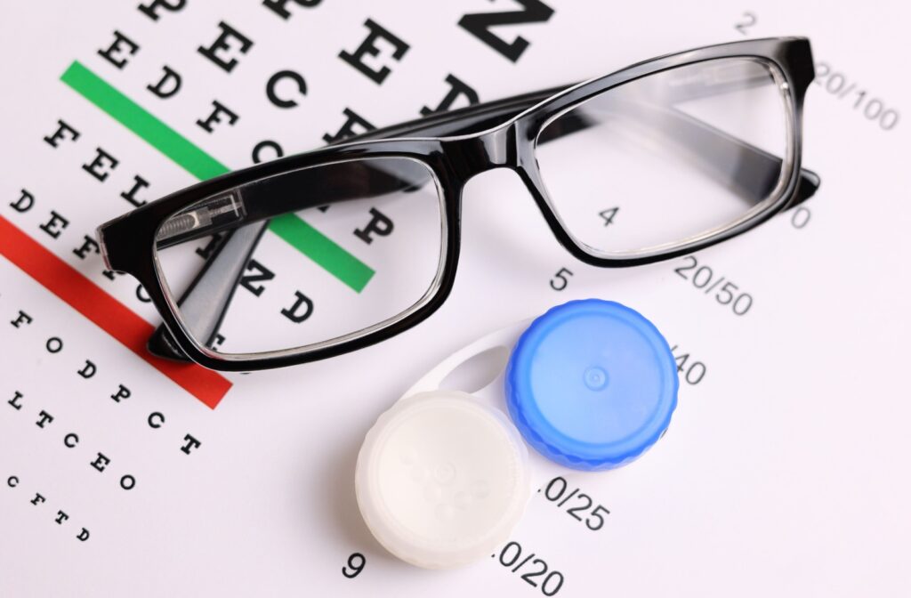 A pair of glasses and a contact lens case placed on an eye chart.