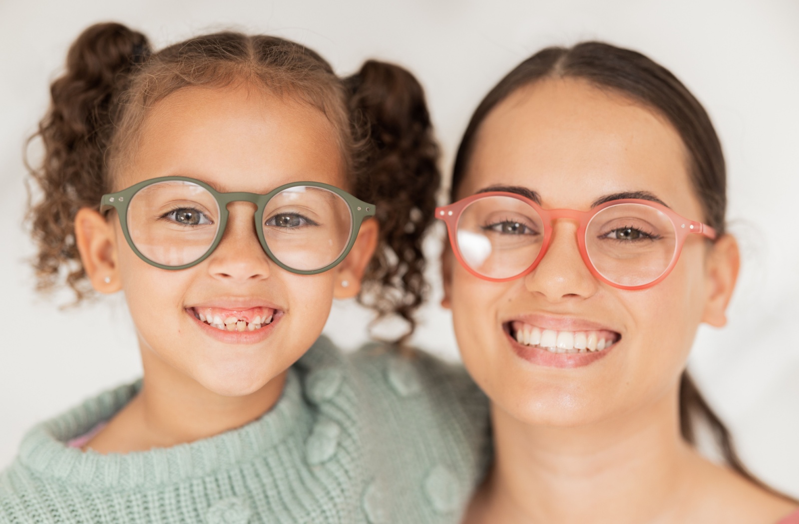 A young child and their parent smiling at the camera wearing matching glasses after a kid's eye exam.