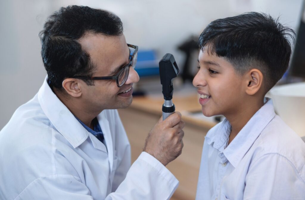 A smiling optometrist holds an eye examination tool while checking a child's vision during an eye exam.