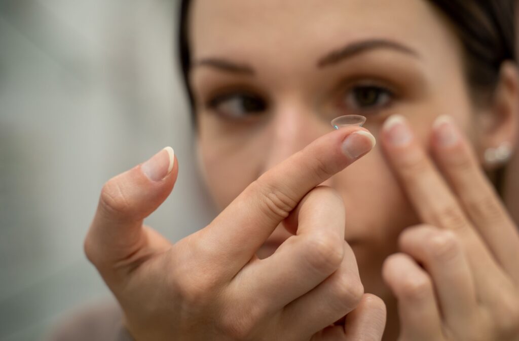 A close up of a person holding a contact lens in front of their eye